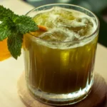 Chilled Japanese Mounjaro detox tea in a glass with mint and orange slice on a wooden table