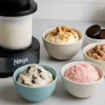 Ninja Creami ice cream maker with four bowls of ice cream featuring Oreo, strawberry, chocolate, and granola toppings.