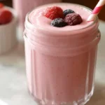 Glass of creamy pink Greek yogurt smoothie topped with frozen berries and a striped straw