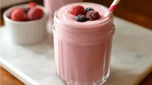 Glass of creamy pink Greek yogurt smoothie topped with frozen berries and a striped straw
