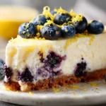 Slice of lemon blueberry cheesecake with fresh blueberries and lemon zest on top