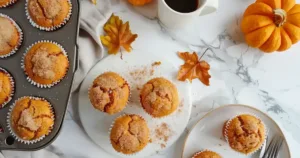 Easy pumpkin muffins in a muffin tin and on a plate, topped with cinnamon sugar, styled with pumpkins and fall decorations