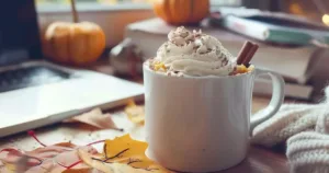 Pumpkin mug cake with whipped cream and cinnamon in a mug, styled for students with books and laptop in the background