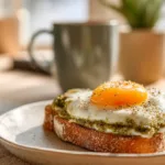 Pesto egg toast with cream cheese served on sourdough with coffee on a student’s breakfast table.