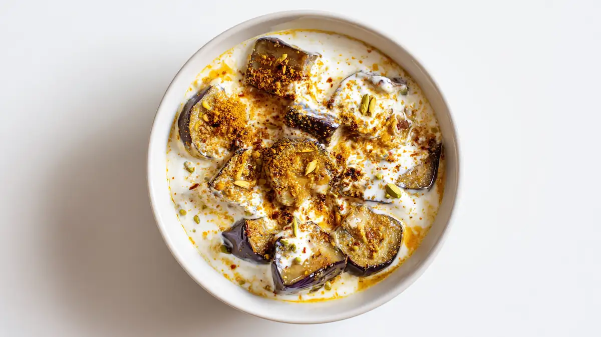Dahi Baingan curry with golden eggplant slices and creamy yogurt sauce on a white desk,