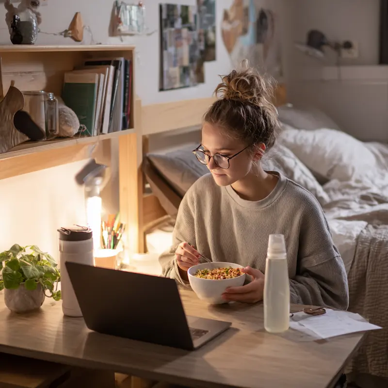 Dorm Microwave Dinners: 15 High-Protein Meals in Under 10 Minutes 3 College student eating a quick microwave dinner while studying in a dorm room, easy high-protein meal for busy nights.