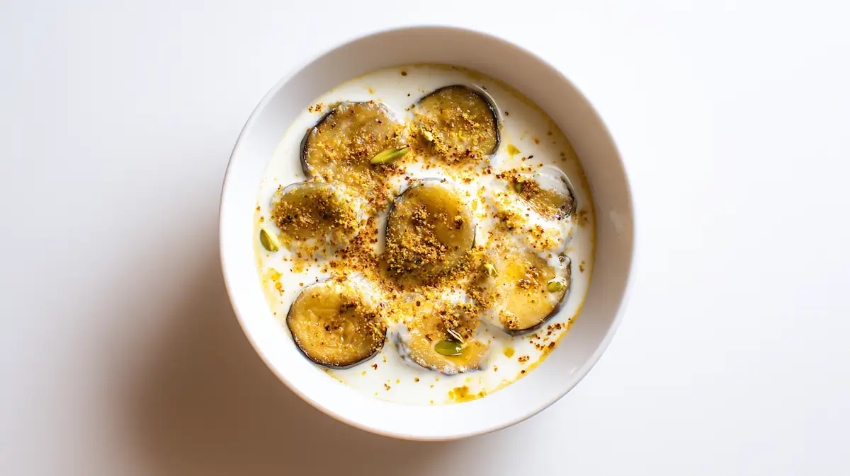 Dahi Baingan curry with golden eggplant slices and creamy yogurt sauce on a white desk, minimal food photo.
