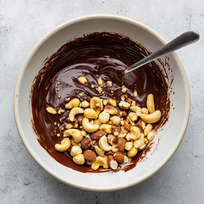 Easy Chocolate Covered Nut Clusters (5-Minute Student Snack You’ll Love!) 2 Melted chocolate in a bowl with mixed nuts ready to be coated for nut clusters.