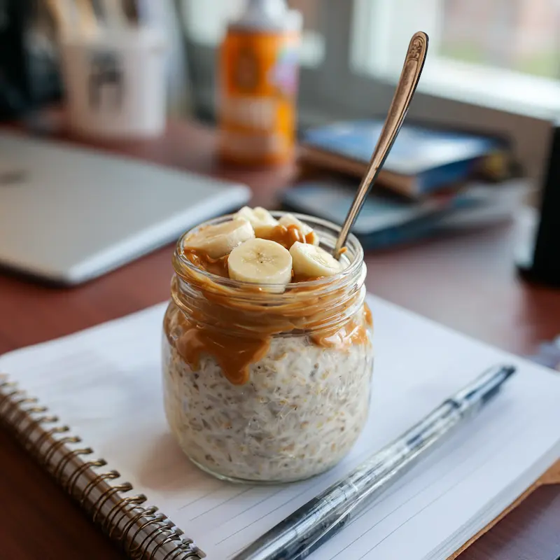 How College Students Can Eat Healthy on a Tight Budget (Without Giving Up Pizza Nights) 3 Jar of overnight oats topped with banana and peanut butter on a dorm desk
