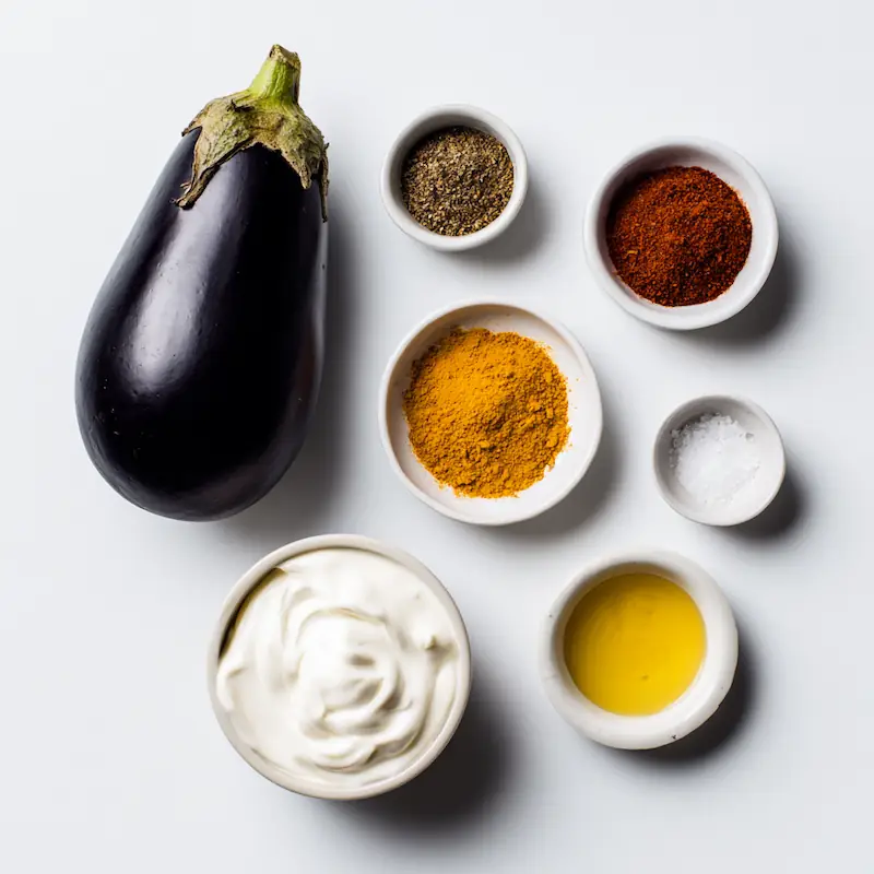 Flatlay of eggplant, yogurt, and Indian spices on a white desk for Dahi Baingan recipe.
