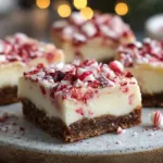 Candy Cane Cheesecake Bars (Baked & No-Bake Holiday Versions for Cozy Nights In) Festive candy cane cheesecake bars on a wooden table with crushed peppermint and fairy lights, creating a cozy Christmas baking atmosphere.