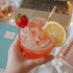 Easy College Mocktails Recipes: 7 Non-Alcoholic Drinks You Can Make in a Dorm College student holding a strawberry mocktail with lemon slice in a cozy dorm setup with laptop and string lights