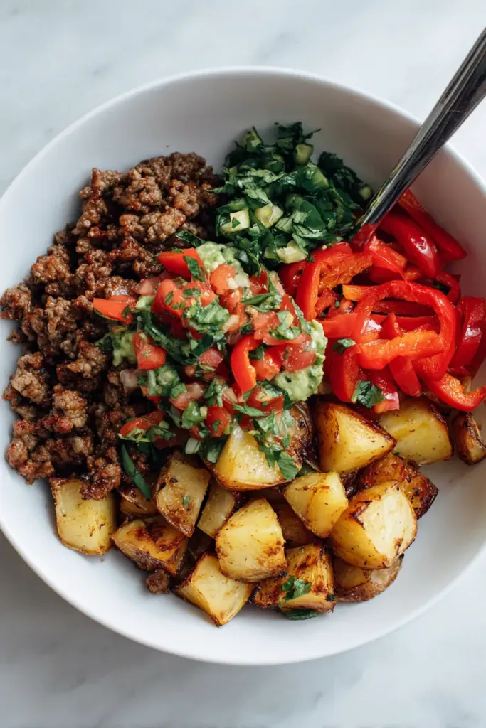 Loaded Potato Taco Bowl Meal Prep (Chicken & Beef Options) 3 Top view of a ground beef loaded potato taco bowl with roasted potatoes, bell peppers, cheese, and pico de gallo on a white table background.