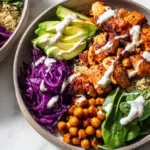 High protein purple sweet potato meal prep bowl with quinoa, chicken, chickpeas, spinach, and tahini yogurt sauce on a white table.