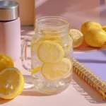 Homemade electrolyte hydration water with lemon slices, honey, and sea salt in a mason jar on a student desk with notebooks and reusable bottle