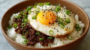 Beef bowl recipe with Korean ground beef over steamed rice, fried egg, sesame seeds, and scallions
