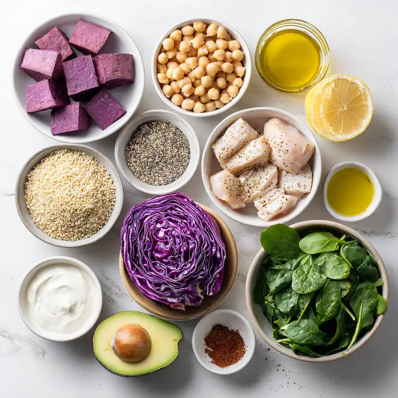 Overhead flatlay of purple sweet potatoes, quinoa, Greek yogurt, tahini, spinach, cabbage, chickpeas, lemon, and seasonings for a healthy meal prep bowl.
