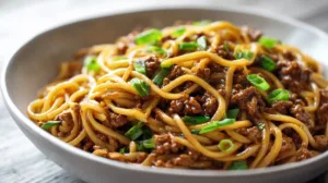 Bowl of Mongolian ground beef noodles with glossy sweet and savory sauce, tender noodles, and sliced green onions