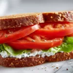 Fresh tomato sandwich with herbed cream cheese on toasted wheat bread, sliced to show juicy red tomatoes and basil.