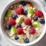 High-protein bircher muesli overnight oats with apple, berries, and almonds in a ceramic bowl.