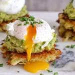 Potato Avocado Toast made with crispy shredded potato hash brown patties topped with mashed avocado and a perfectly poached egg with runny yolk on a white marble board.