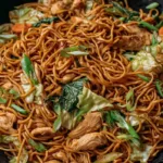 Chicken chow mein recipe with homemade sauce featuring tender chicken, stir-fried noodles, cabbage, carrots, and green onions in a wok.