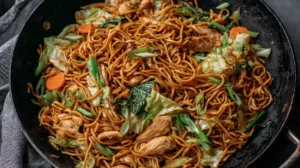 Chicken chow mein recipe with homemade sauce featuring tender chicken, stir-fried noodles, cabbage, carrots, and green onions in a wok.