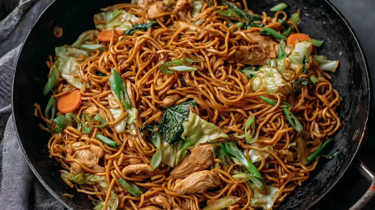 Chicken chow mein recipe with homemade sauce featuring tender chicken, stir-fried noodles, cabbage, carrots, and green onions in a wok.