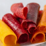 Homemade 3 ingredient fruit leather recipe in the oven rolled into strips on parchment paper