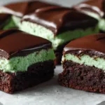 Fudgy mint brownies layered with green mint frosting and topped with glossy chocolate ganache, cut into clean squares on parchment paper