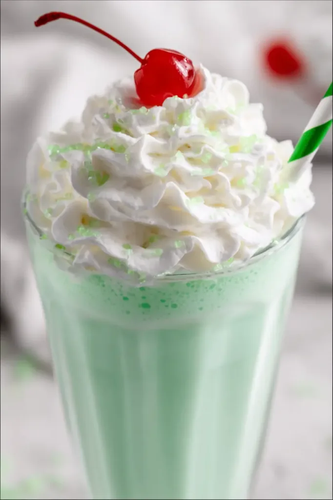 Homemade shamrock shake topped with whipped cream and cherry in a clear glass.