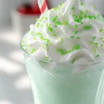 Creamy homemade shamrock shake topped with whipped cream and green sprinkles in a tall clear glass.