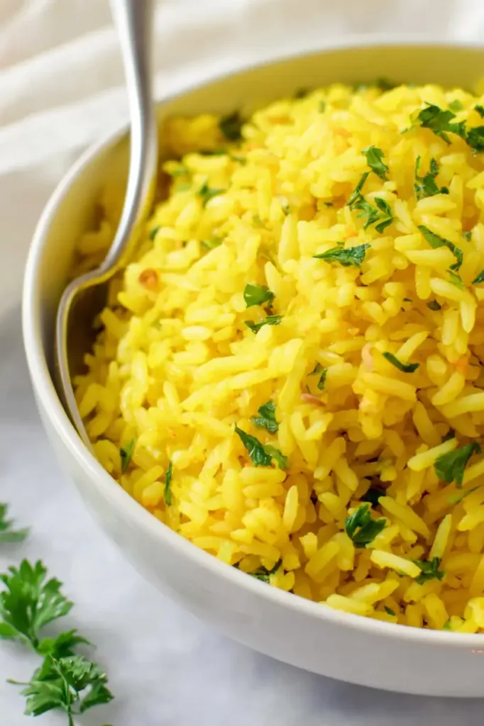 Bowl of fluffy golden turmeric rice garnished with parsley in a white bowl
