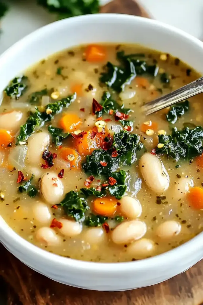 Bowl of Tuscan white bean soup with cannellini beans, kale, carrots, and red pepper flakes in natural light.