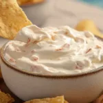 Creamy viral boat dip recipe served in a white bowl with shredded cheese and diced tomatoes, surrounded by tortilla chips on a bright summer table.