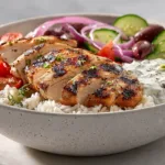 Greek Chicken Bowls with juicy baked chicken, rice, fresh vegetables, olives, and creamy homemade tzatziki in a Mediterranean bowl