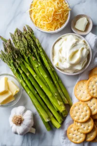 Ingredients for asparagus casserole including fresh asparagus, shredded cheddar cheese, Ritz crackers, butter, garlic, and sour cream
