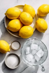Fresh lemons, granulated sugar, and water arranged on a marble surface for old fashioned lemonade recipe