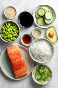 Flat lay of ingredients for teriyaki salmon sushi bowl including raw salmon, sushi rice, avocado, cucumber, edamame, soy sauce, and rice vinegar.