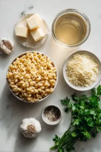 Flat lay of ingredients for chicken broth pasta including dry pasta, chicken broth, butter, garlic, and parmesan cheese on a light surface.