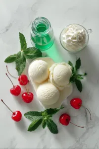 Vanilla ice cream, milk, mint extract, green food coloring, whipped cream, and cherries arranged for a shamrock shake recipe.