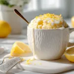 Lemon Mug Cake (Easy Microwave Recipe in 2 Minutes) Fluffy lemon mug cake in a white mug topped with lemon glaze and fresh zest on marble counter