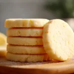 Buttery lemon shortbread cookies sliced and baked, arranged on a wooden board with a soft golden color and melt-in-your-mouth texture.