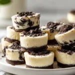 Mini Oreo Cheesecake Bites (Easy 30 Minute Recipe) Stacked mini Oreo cheesecake bites showing creamy cheesecake filling with Oreo cookie layers on a white plate in bright natural light.