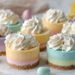 No Bake Easter Mini Cheesecakes Easy Recipe Pastel layered no bake Easter mini cheesecakes topped with whipped cream and sprinkles on a light marble surface.