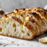 Golden no knead rosemary garlic bread loaf with crispy crust and soft airy crumb on rustic wooden table