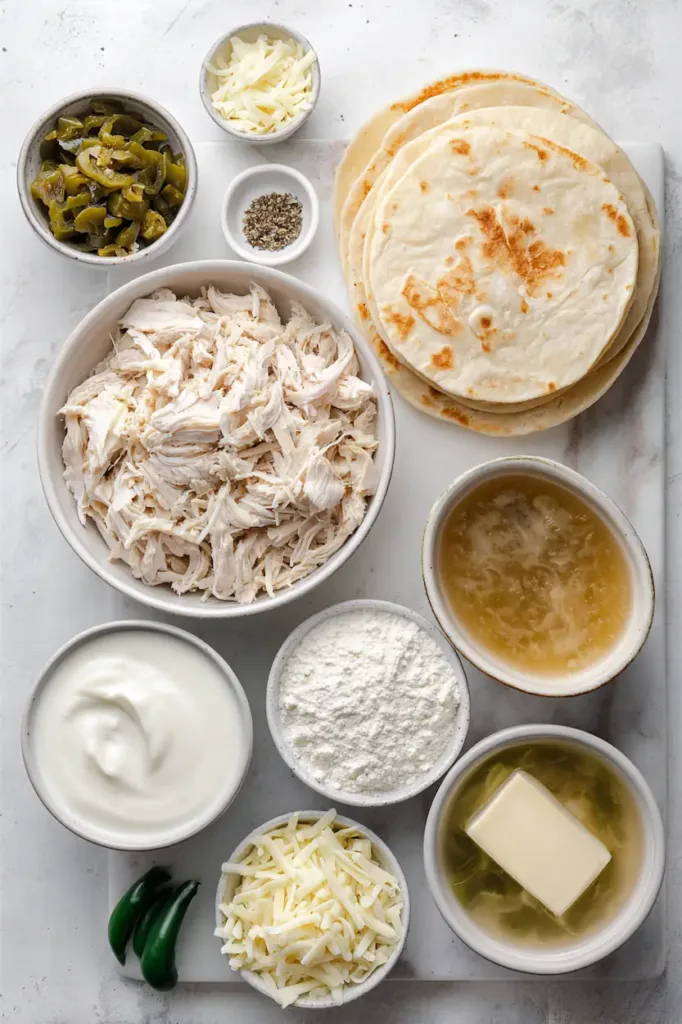 Chicken Enchiladas with Sour Cream White Sauce 3 Flat lay of ingredients for chicken enchiladas with sour cream white sauce including shredded chicken, tortillas, sour cream, cheese, butter, flour, broth, and green chiles
