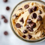 Jar of edible cookie dough for one topped with chocolate chips and a spoon, creamy no-bake dessert made from a simple edible cookie dough recipe.