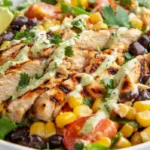 Bowl of high protein Southwest chicken salad with grilled chicken, black beans, corn, cherry tomatoes, avocado, and romaine lettuce in natural light.