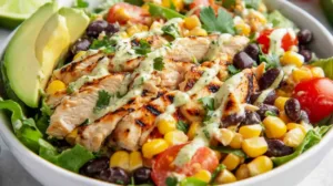 Bowl of high protein Southwest chicken salad with grilled chicken, black beans, corn, cherry tomatoes, avocado, and romaine lettuce in natural light.